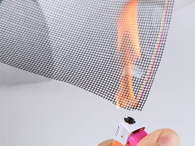 A hand is burning a piece of fiberglass insect screen.