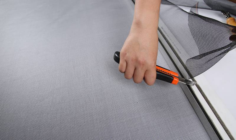 A worker is trim excess screens with knife.